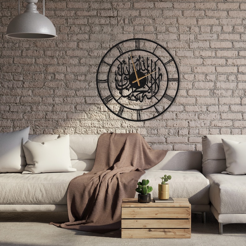 K&ouml;nnte beinhalten: Eine schwarze Metall-Wanduhr mit r&ouml;mischen Ziffern und arabischer Kalligraphie. Die Uhr hat goldfarbene Zeiger und ist an einer Backsteinmauer befestigt. Die Uhr ist ein dekoratives Element f&uuml;r ein Wohnzimmer oder die Inneneinrichtung.