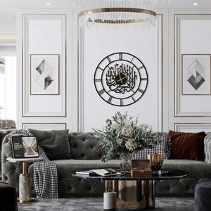 K&ouml;nnte beinhalten: Ein Wohnzimmer mit einem grauen Sofa, einem runden Couchtisch und einer dekorativen Wanduhr mit arabischer Kalligraphie. Der Raum ist mit gerahmter Kunst, einem Blumenarrangement und einem Beistelltisch aus Marmor dekoriert.