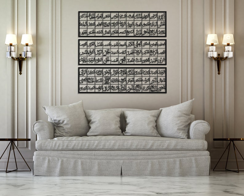 May include: Three black metal framed wall art pieces with Arabic calligraphy in a modern living room setting with a gray couch and two lamps on either side of the art.