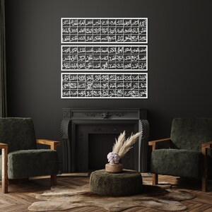 May include: Three white metal wall art pieces with Arabic calligraphy in a dark room with a fireplace and two green armchairs.