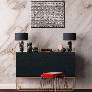 May include: A black console table with three drawers and gold metal legs. Two black lamps with black marble bases are on the table. A red velvet stool with a gold metal frame is in front of the table. A black framed print with Arabic calligraphy is on the wall behind the table.