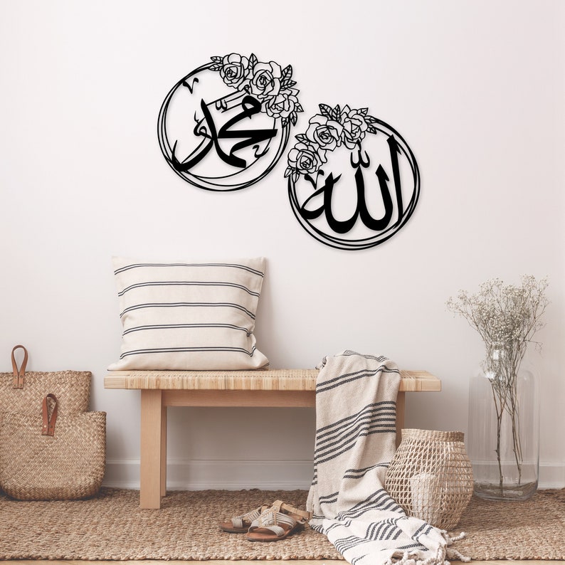 K&ouml;nnte beinhalten: Zwei schwarze Wanddekorationen aus Metall mit floralen Akzenten. Die St&uuml;cke zeigen die arabischen W&ouml;rter "Allah" und "Muhammad" in einer dekorativen Schrift.