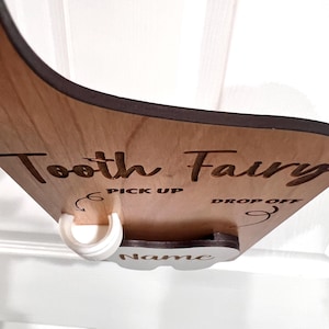 May include: Wooden tooth fairy box with a white plastic tooth holder. The box has the words "Tooth Fairy" and "Pick Up" and "Drop Off" written on it. There is a space for a name on the box.