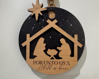 May include: Wooden Christmas ornament featuring a nativity scene silhouette. The ornament has a black background with white stars, a wooden star, and the text "FOR UNTO US A Child is born". Includes a wooden bead and twine for hanging.