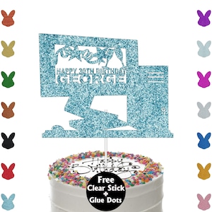 May include: A blue glitter cake topper with the text "HAPPY 30TH BIRTHDAY GEORGE". The topper features a design with stars, champagne glasses, and a computer-like shape. It is placed on a white cake with colourful sprinkles.