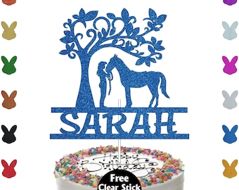 May include: A blue glitter cake topper featuring a silhouette of a person and a horse under a tree, with the name "SARAH" below. The topper is on a cake with colorful sprinkles and the words "Happy Birthday".