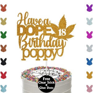 May include: A gold glitter cake topper with the words "Have a DOPE Birthday poppy 18" and a cannabis leaf design. The topper is on a white cake with colorful sprinkles and the words "Happy Birthday" on the cake.