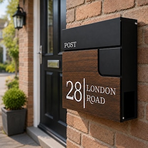 May include: A rectangular wall-mounted post box featuring a matte black metal frame and a dark wood-grain front panel. The word POST is printed in white on the top section, while the number 28 and the text LONDON ROAD are displayed in white.