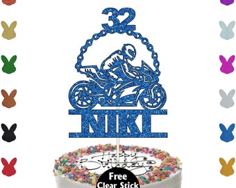 May include: A blue glitter motorcycle cake topper with the name "NIKI" and the number "32". The topper features a motorcycle racer design and is placed on a white cake with colorful sprinkles. The cake says "Happy Birthday".