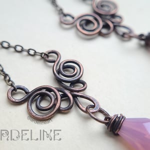May include: A pair of earrings with a delicate copper wire design and a light purple gemstone dangle. The earrings are connected by a chain.