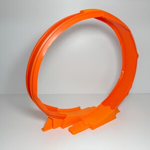 May include: A bright orange plastic toy loop-the-loop track for toy cars. The track forms a complete circle with a ramp at the bottom. The toy is designed for high-speed fun and is made of durable plastic.