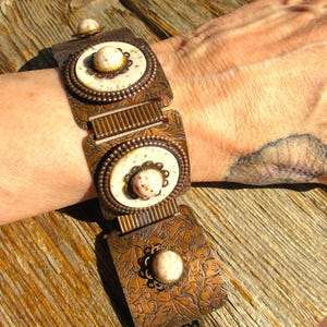 May include: A vintage copper bracelet with an ornate floral design. The bracelet features three rectangular links with cream-colored oval accents and a central stone. The bracelet is approximately 7 inches long.
