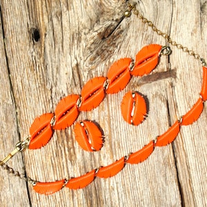 May include: A jewelry set consisting of a necklace and a bracelet, both featuring bright orange, leaf-shaped components linked by gold-tone metal chains. The set also includes two matching orange leaf-shaped earrings with gold-tone metal hardware.