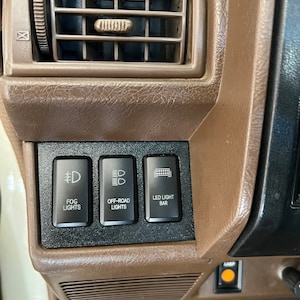 May include: Close-up of a car's dashboard with three black toggle switches labeled "Fog Lights", "Off-Road Lights", and "LED Light Bar".