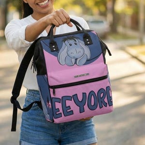 May include: A backpack with a cartoon image of Eeyore from Winnie the Pooh. The backpack is primarily pink and blue, with the name "Eeyore" printed on the front. The text "This is an original design of BERRY BROTHERS SHOP" is in the upper right corner.