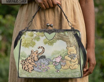 May include: A structured handbag featuring a light green background with a printed illustration of Tigger, Eeyore, Piglet, and Winnie the Pooh. The bag has a dark metal kiss-lock closure, a top handle, and black side straps. Text reads: This is an original design of BERRY BROTHERS SHOP.
