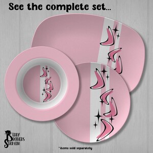 May include: A pink dinnerware set including a rectangular platter, a round bowl, and a round plate. Each piece features a white vertical stripe decorated with black and pink boomerang shapes and four-pointed star accents. Text reads: See the complete set.