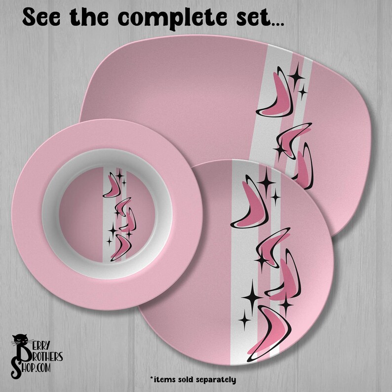 May include: A pink dinnerware set including a rectangular platter, a round bowl, and a round plate. Each piece features a white vertical stripe decorated with black and pink boomerang shapes and four-pointed star accents. Text reads: See the complete set.