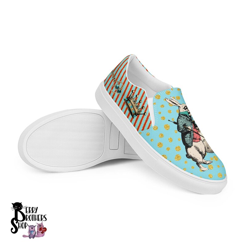 May include: White slip-on canvas shoes with a blue and gold pattern featuring a white rabbit wearing a waistcoat and holding a pocket watch. The pattern also includes a crown and other details.