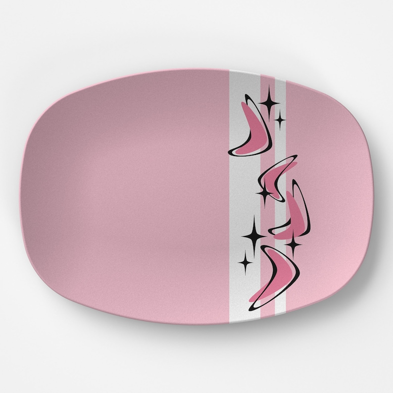May include: A pink oval serving platter with a retro design. The platter features a vertical white and gray stripe with black and pink boomerang shapes and starburst accents. The rest of the platter is solid pink.