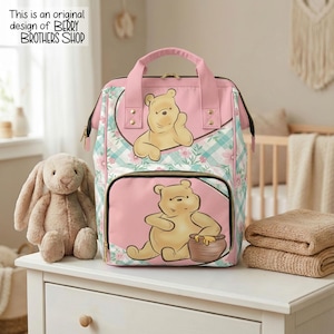 May include: A pink and teal plaid backpack featuring Winnie the Pooh illustrations on the front pockets. The bag has pink top handles, gold-tone zippers, and a floral pattern. Text in the corner reads: This is an original design of BERRY BROTHERS SHOP.