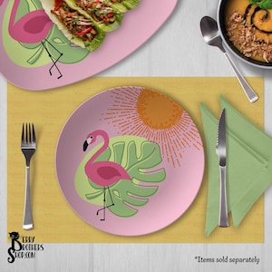May include: Pink plates with a flamingo design, a green leaf, and an orange sunburst. The plates are on a yellow placemat with a fork, knife, and green napkin. The image includes the text "Berry Brothers Shop.com".