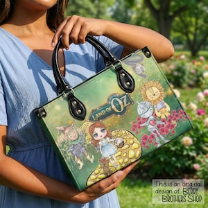 May include: Green tote bag with illustrations of characters from The Wizard of Oz, including Dorothy, the Scarecrow, Tin Man, and Lion. The bag has black handles and the words "Land of Oz" are printed on the front.