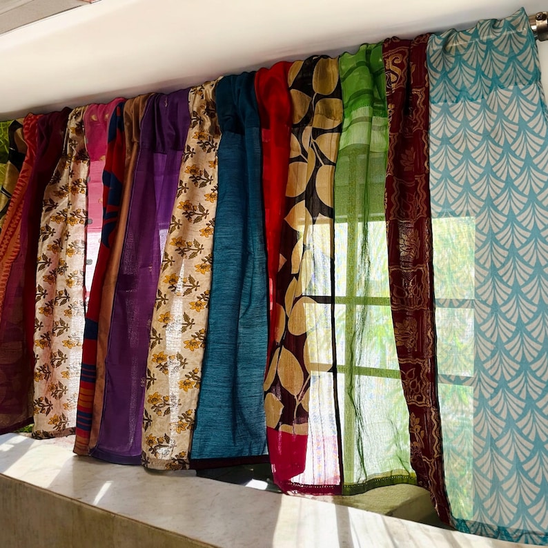May include: A set of colorful curtains made from repurposed fabric. The curtains are a mix of different patterns and textures, including floral, geometric, and paisley designs. The curtains are hung on a window and are letting in natural light.