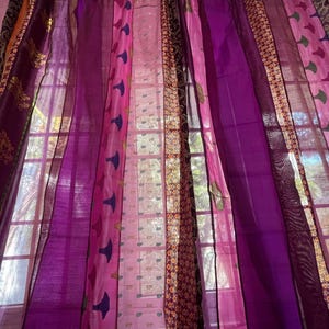 May include: A set of sheer curtains in various shades of purple and pink, with intricate patterns and designs. The curtains are hung in a window and allow light to filter through.