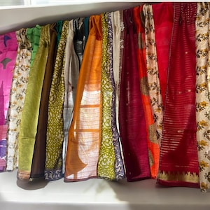 May include: A collection of colorful fabric panels, likely used as curtains or wall decor. The panels are made of various materials, including silk, cotton, and linen, and feature a variety of patterns and textures. The colors range from deep reds and oranges to light greens and blues.