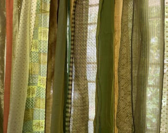 May include: A collection of sheer curtains in various shades of green and brown with different patterns. The curtains are hanging in a window and are illuminated by natural light.