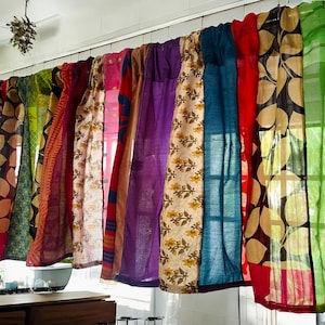 May include: A collection of colorful fabric curtains with various patterns and textures. The curtains are made of different materials, including silk, cotton, and linen. They are hung on a white wall and are arranged in a cascading pattern.