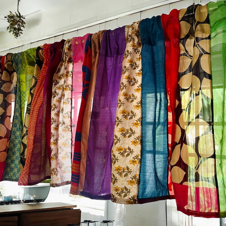 May include: A collection of colorful fabric curtains with various patterns and textures. The curtains are made of different materials, including silk, cotton, and linen. They are hung on a white wall and are arranged in a cascading pattern.
