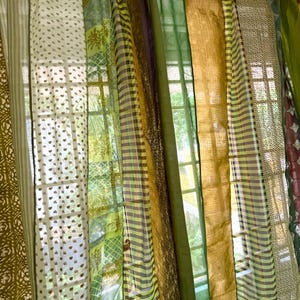 Puede incluir: Un conjunto de cortinas transparentes en varios tonos de verde y dorado. Las cortinas están hechas de diferentes telas, incluyendo voile, a rayas y estampadas. Las cortinas están colgadas en una ventana y dejan entrar la luz natural.