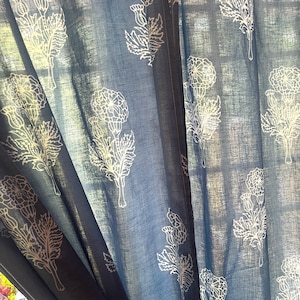 May include: Blue and white floral patterned curtain panels. The curtains feature a repeating design of stylized white flowers and leaves against a blue background. The fabric appears to be lightweight and allows light to filter through.
