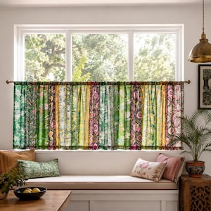 May include: A window curtain featuring a patchwork design of vertical fabric panels in various shades of green, yellow, and pink with intricate floral and geometric patterns, suspended from a simple metal rod across a large window frame.