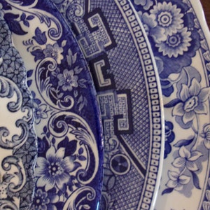 May include: Three ceramic plates featuring intricate blue and white patterns. The designs include floral motifs, scrolling vines, and geometric borders with scalloped edges. The plates are layered, showcasing detailed transferware illustrations.