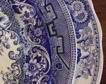 May include: Three ceramic plates featuring intricate blue and white patterns. The designs include floral motifs, scrolling vines, and geometric borders with scalloped edges. The plates are layered, showcasing detailed transferware illustrations.
