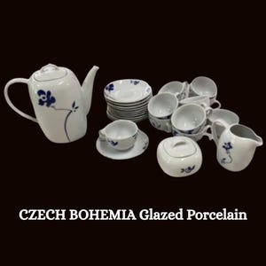 Può includere: Un servizio da tè in porcellana smaltata Czech Bohemia bianca con decorazioni floreali blu. Il set include una teiera, tazze, piattini, una zuccheriera e una lattiera. Il testo "CZECH BOHEMIA Glazed Porcelain" è in basso.