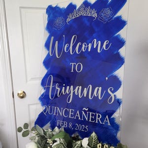 Op de afbeelding: Een blauw en wit welkomsbord voor een quincea&ntilde;era. Het bord zegt "Welkom bij Ariyana's Quincea&ntilde;era 8 februari 2025".