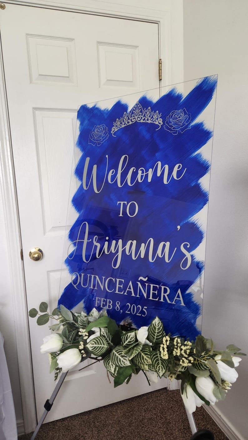 Op de afbeelding: Een blauw en wit welkomsbord voor een quincea&ntilde;era. Het bord zegt "Welkom bij Ariyana's Quincea&ntilde;era 8 februari 2025".