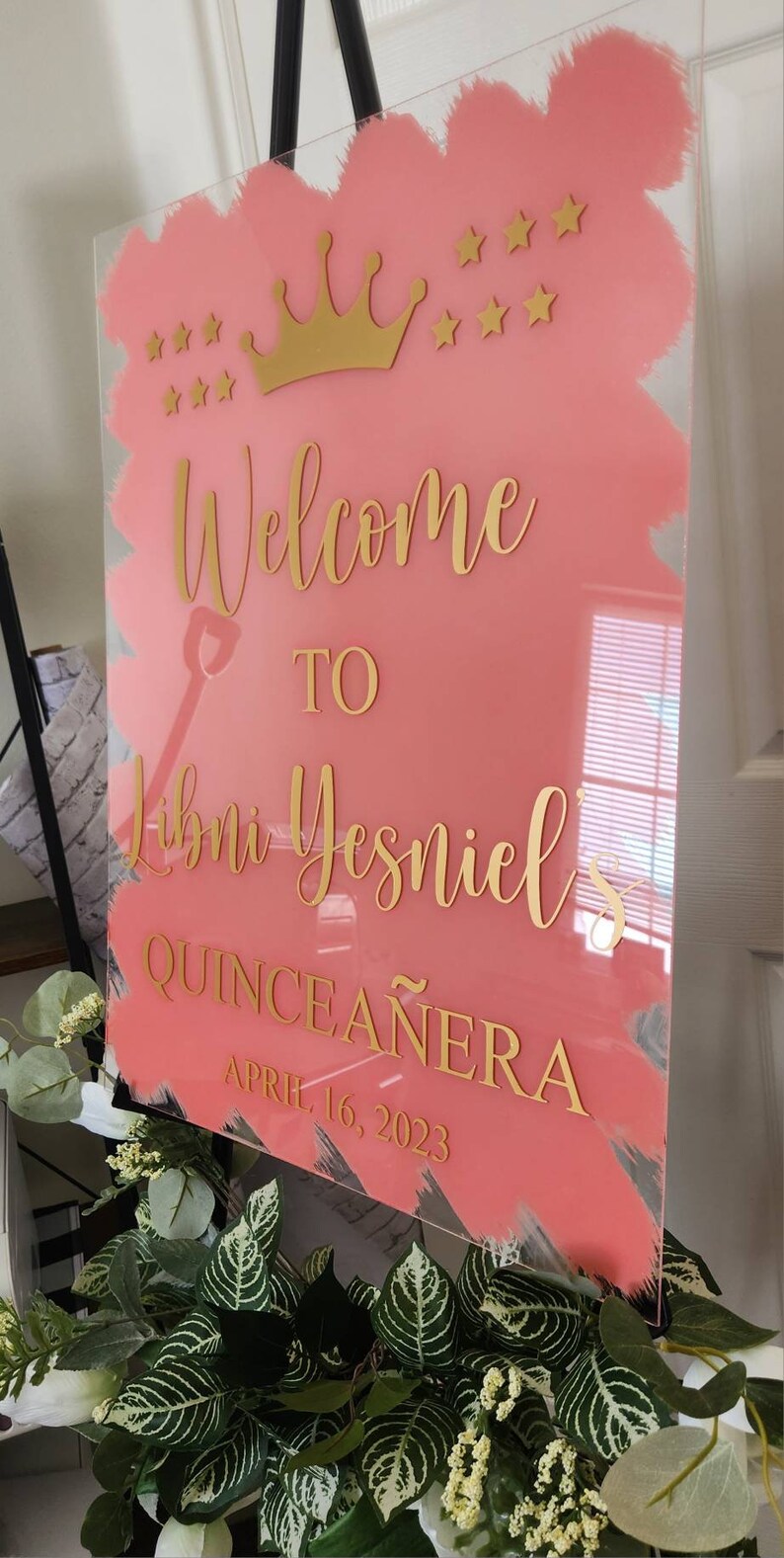 May include: A pink acrylic welcome sign with gold lettering and a gold crown. The sign reads "Welcome to [Name]'s Quincea&ntilde;era April 16, 2023".