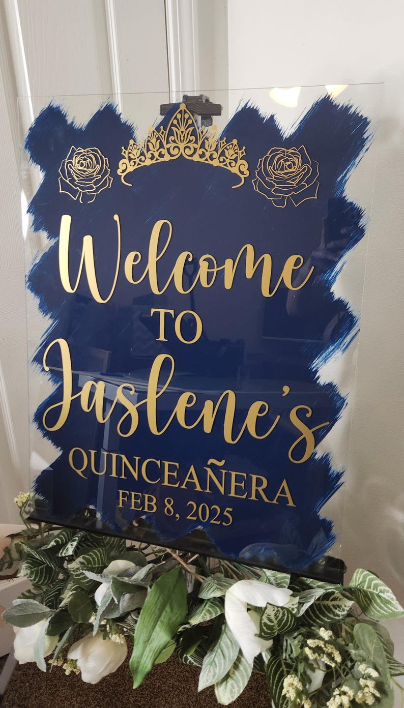 Op de afbeelding: Een blauw en gouden welkomsbord voor een Quincea&ntilde;era. Het bord zegt "Welkom bij Jaslene's Quincea&ntilde;era 8 februari 2025".