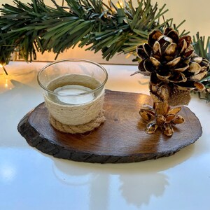 May include: A wooden slice with a small glass candle holder wrapped in twine and a pine cone sculpture made of natural materials.