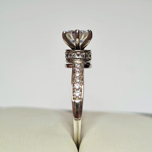 May include: A silver ring featuring a large, clear, round diamond set in a flower-shaped setting. The band is also set with smaller diamonds.