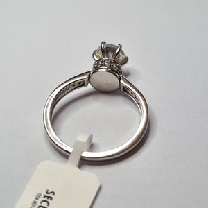 May include: A silver ring featuring a large clear cubic zirconia stone set in a crown-like design. The ring is displayed on a white background with a white tag that reads "SECURITY TAG ITEM NOT RETURNABLE IF REMOVED".