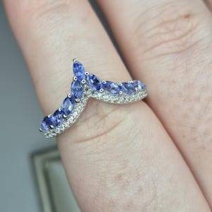 May include: A silver ring with a V-shaped band set with blue marquise-shaped gemstones and smaller clear round gemstones.
