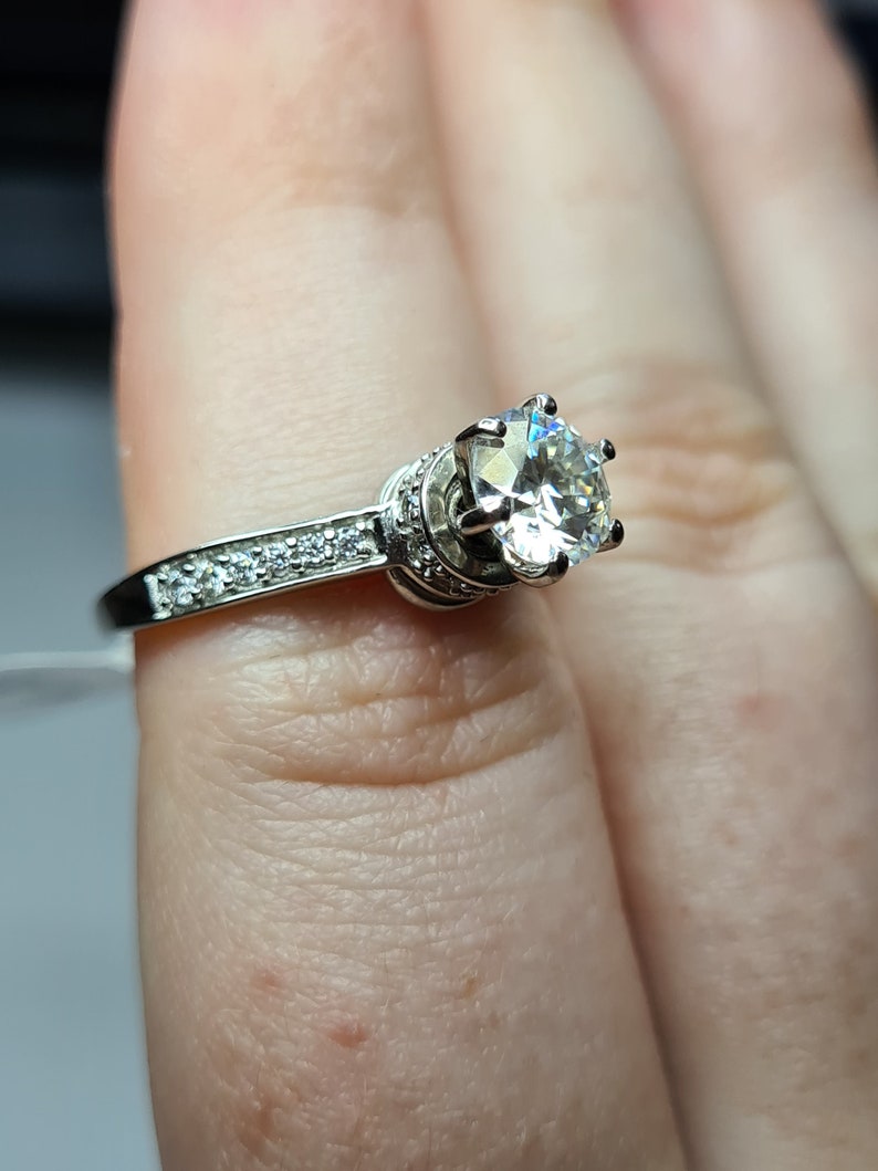 May include: A silver ring with a large, clear, round gemstone surrounded by smaller gemstones. The ring is on a finger.