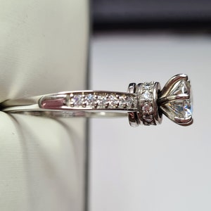 May include: A silver engagement ring with a large, round, clear centre stone and a band of smaller, clear stones.