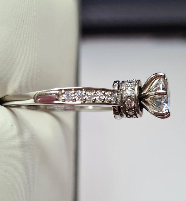 May include: A silver engagement ring with a large, round, clear centre stone and a band of smaller, clear stones.